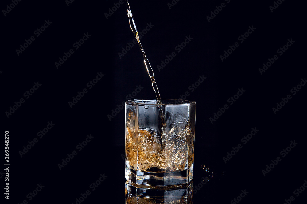 Whiskey pouring into glass with ice isolated on black background.. Whiskey pouring into glass with ice isolated on black background..