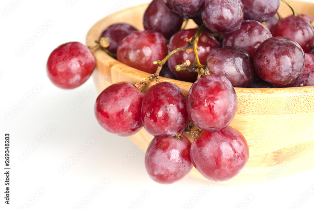 Isolated juicy clusters of large red grapes coiled from a wooden bowl