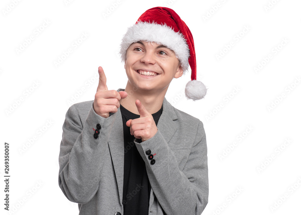 Portrait of smiling teen boy with Christmas hat. Teenager wearing grey suit, pointing and looking upwards. Holiday concept - happy cute child isolated on white background. Portrait of smiling teen boy with Christmas hat. Teenager wearing grey suit, pointing and looking upwards. Holiday concept - happy cute child isolated on white background.