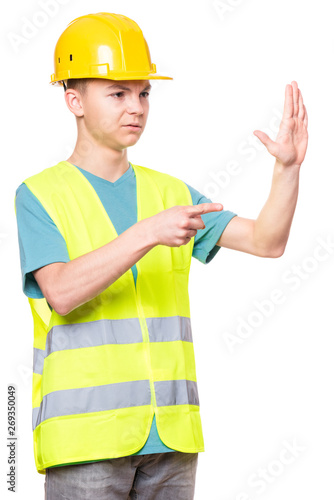 Funny Handsome Teen Boy wearing Safety Jacket and yellow Hard Hat. Portrait of Happy Child Makes Hands Gesture and Looking away, isolated on white background.