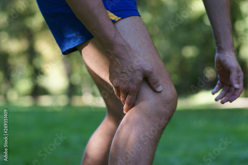 Muscle injury - man with sprain thigh muscles after jogging in park. Athlete in sports shorts clutching his thigh muscles.