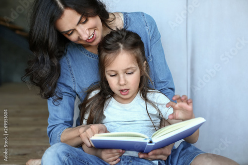 Happy mother with daughter reading book at home