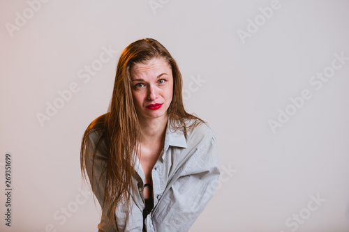 Sad young blonde girl with red lips on a gray background. Human emotion facial expression body language.