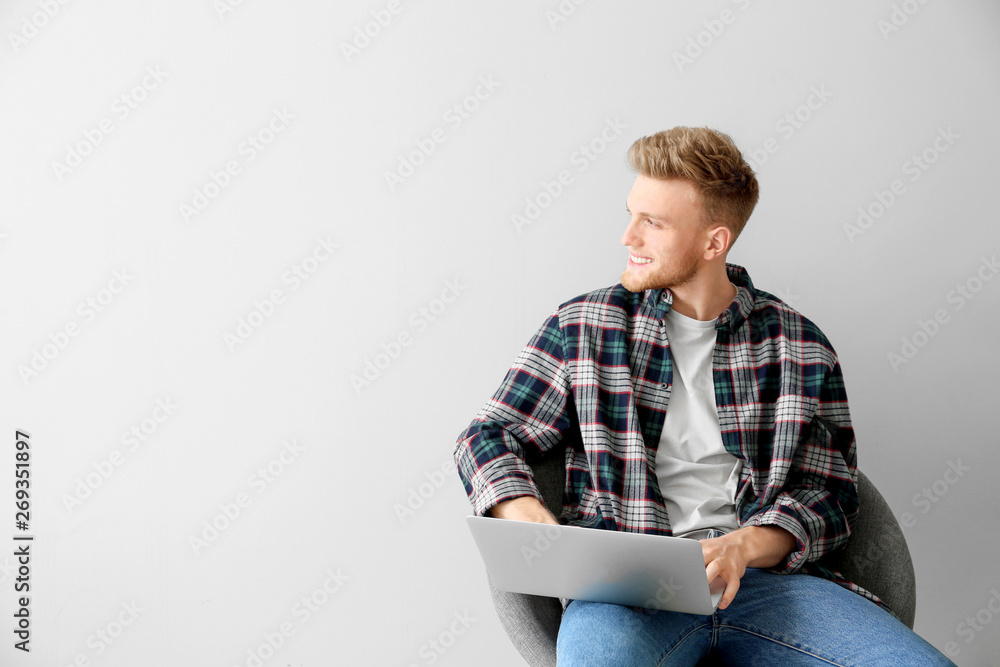 Handsome young man with laptop sitting on chair against light background Handsome young man with laptop sitting on chair against light background