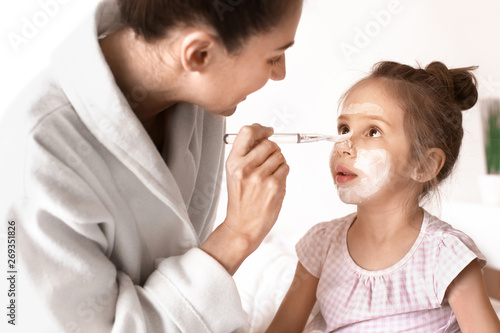 Mother applying mask onto daughter's face at home