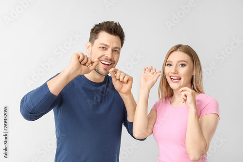 Man and woman flossing teeth on light background