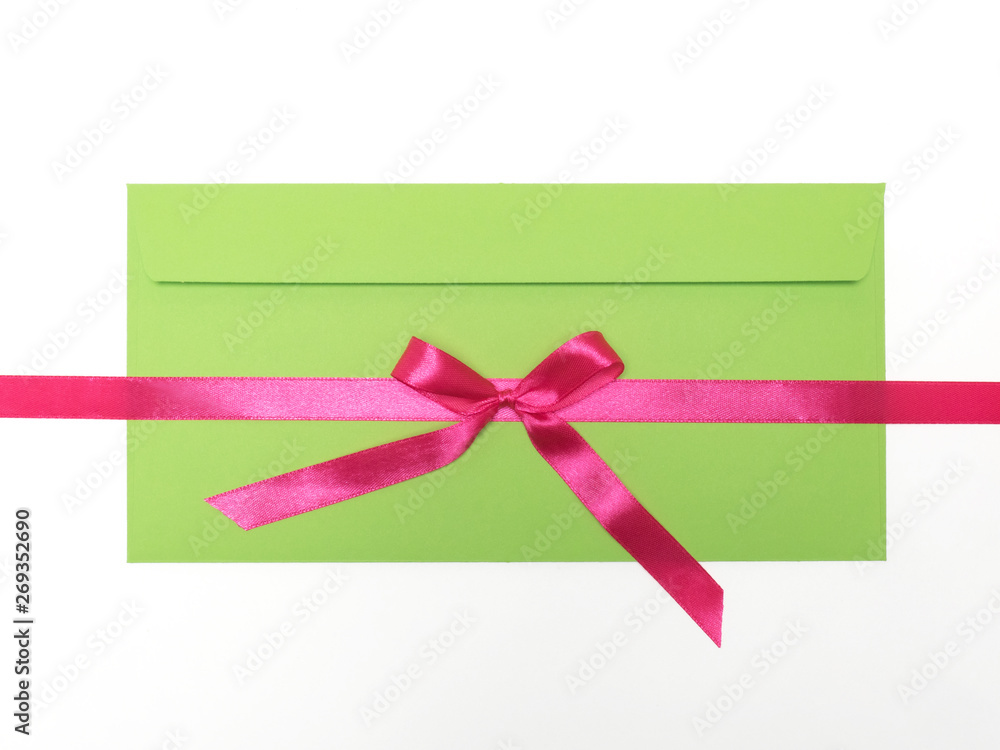 Pink satin ribbon horizontally with bow with green envelope on white background Pink satin ribbon horizontally with bow with green envelope on white background