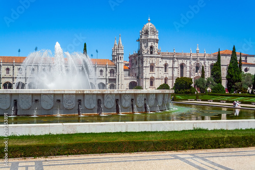Lisbon, Portugal. Jeronimos Monastery or Abbey aka Santa Maria de Belem seen from Jardim da Praca do Imperio Garden and Square. Fountain with water jets spray