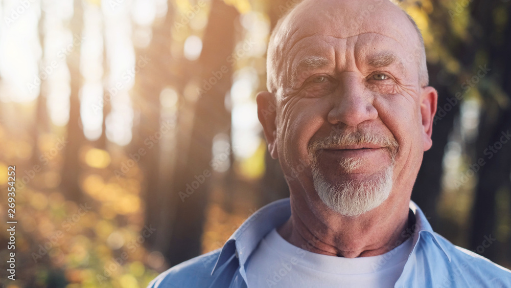 Portrait of senior man with a beard smiling while standing outside in sunlight. Portrait of senior man with a beard smiling while standing outside in sunlight.
