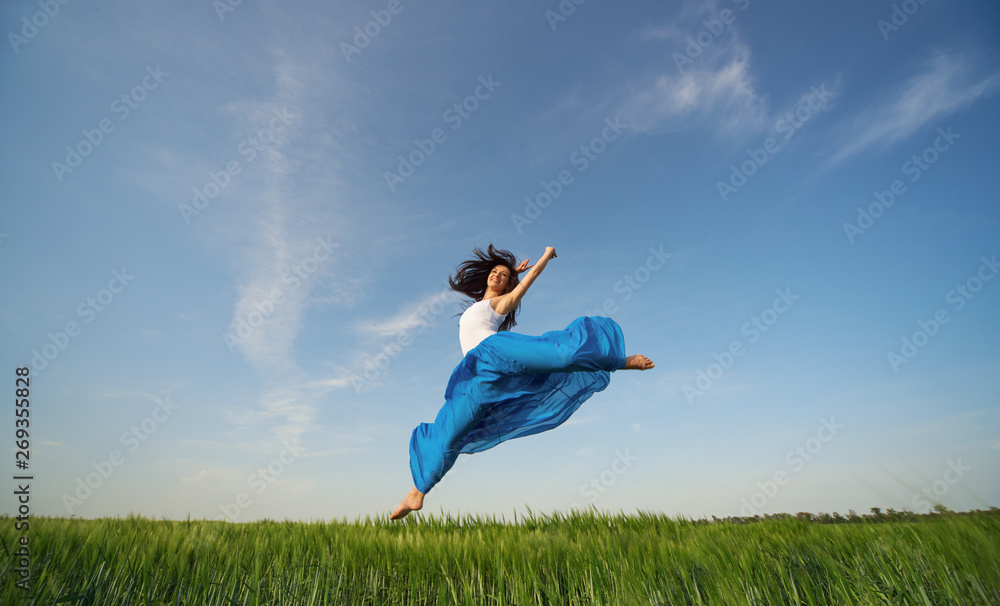 Flying dancer in the air. Happy woman ballerina in blue fabric skirt making a big jump on Green field. Summer or Spring concept Flying dancer in the air. Happy woman ballerina in blue fabric skirt making a big jump on Green field. Summer or Spring concept