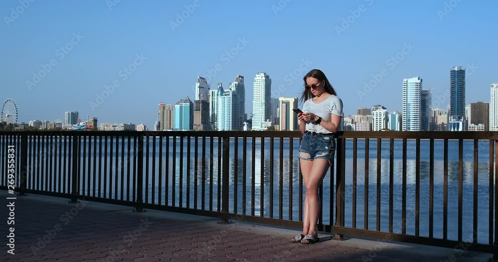 Girl on the background of the big city and the Bay holding a smartphone in sunglasses Girl on the background of the big city and the Bay holding a smartphone in sunglasses