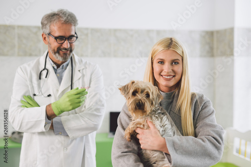 woman holding her dog at veterinary clinic. veterinarian in blurred background