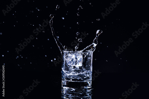 Isolated cold water in a glass with splash and cubes of ice on black background, brandy in a glass