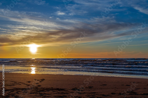 Sand beach with endless horizon and foamy waves under the bright sundown with yellow colors and clouds above the sea