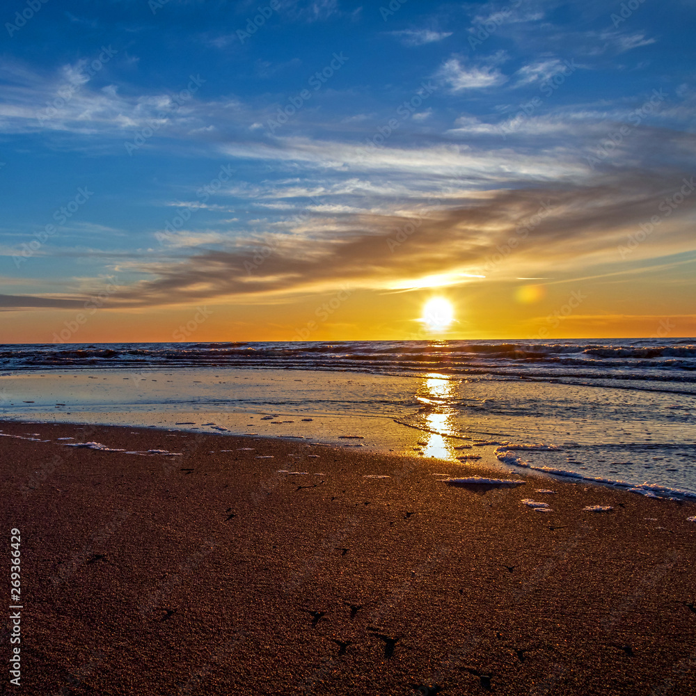 Sand beach with endless horizon and foamy waves under the bright sundown with yellow colors and clouds above the sea Sand beach with endless horizon and foamy waves under the bright sundown with yellow colors and clouds above the sea