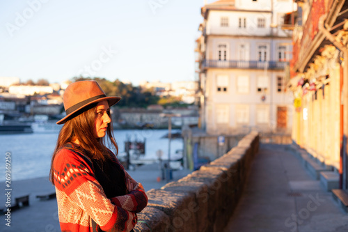 Young woman with long hair walking on city street at sunrise, wearing hat and coat, enjoying happy pleasant moment of her vacations