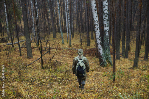 Traveler in camouflage with a backpack is walking in the middle of the autumn forest. Extreme travel. Survival in the wild.