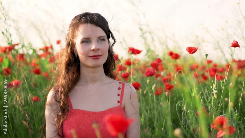 Close up, slow motion, portrait of an attractive woman in a red sundress with hair developing in the wind on the poppy field Close up, slow motion, portrait of an attractive woman in a red sundress with hair developing in the wind on the poppy field