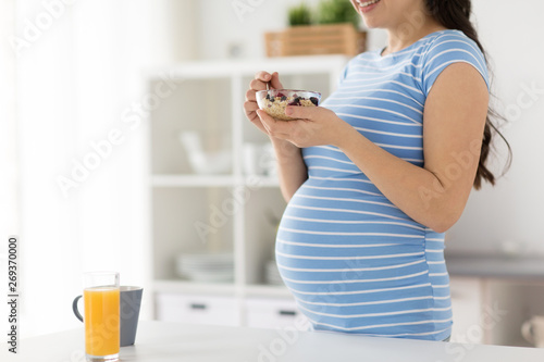 pregnancy, diet and people concept - close up of happy pregnant woman eating fruit muesli at home kitchen