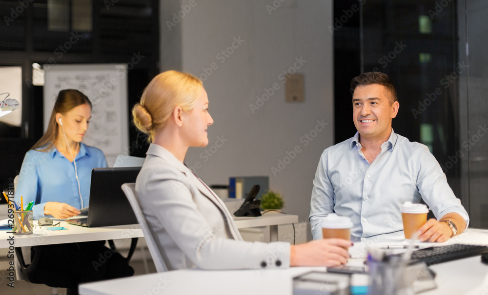 Obraz premium business, deadline and technology concept - businesswoman and businessman talking and drinking coffee late at night office