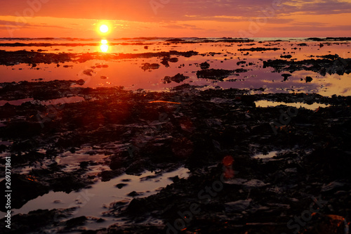 Beautiful red sunset. The sun is setting in the sea. Reflection in the sea  rocky shore. Sun rays.