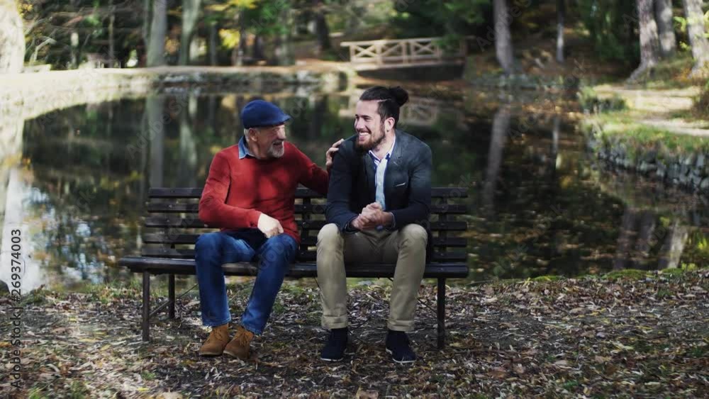 Senior father and his son sitting on bench by lake in nature, talking. Senior father and his son sitting on bench by lake in nature, talking.