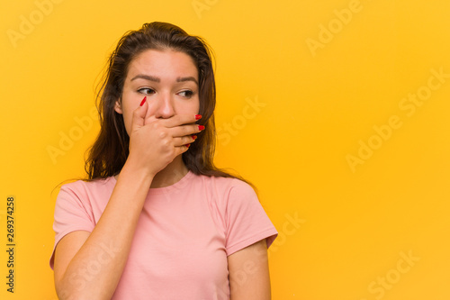 Young european woman isolated over yellow background thoughtful looking to a copy space covering her mouth with hand.