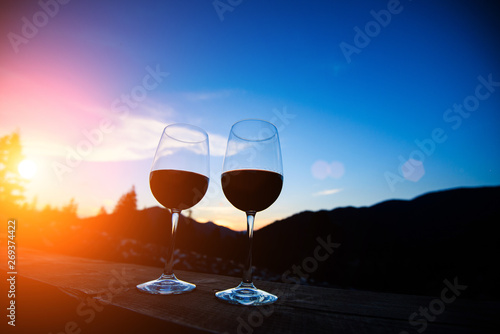 Two glasses of wine at sunset dramatic sky on mountain landscape background