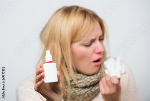 Dispenser bottle. Sick woman spraying medication into nose. Treating common cold or allergic rhinitis. Cute woman nursing nasal cold or allergy. Unhealthy girl with runny nose using nasal spray