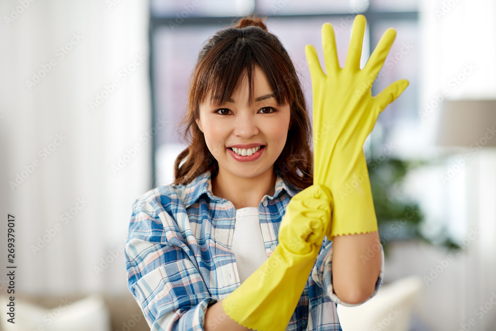 cleaning, housework and hand protection concept - asian woman in protective rubber gloves at home cleaning, housework and hand protection concept - asian woman in protective rubber gloves at home