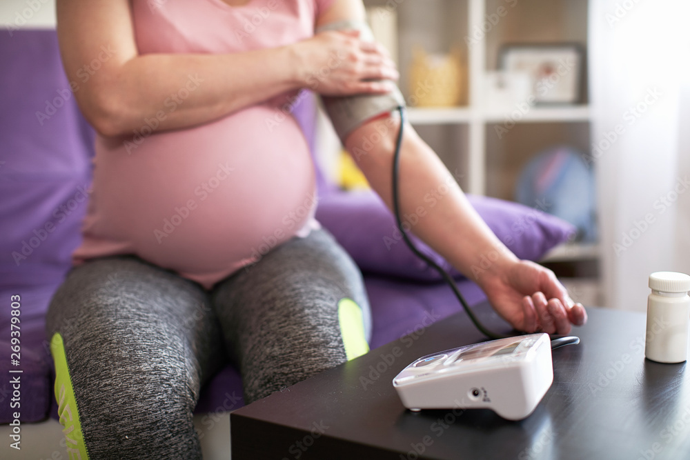 Fototapeta premium a woman measures blood pressure with an electronic pressure gauge, headache during pregnancy, poor health. selective focus on medical equipment