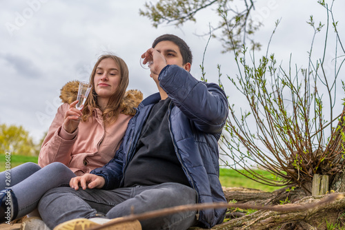 A young couple is sitting in nature drinking water from champagne glasses