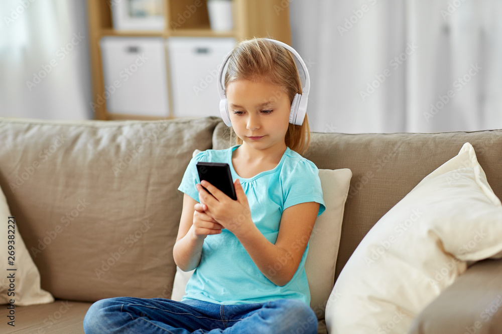 childhood, technology and leisure concept - little girl in headphones listening to music at home childhood, technology and leisure concept - little girl in headphones listening to music at home