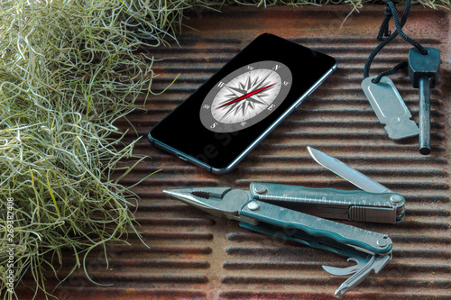 multi tool with flint and celll phone with compass app on a rusty griddle background photo