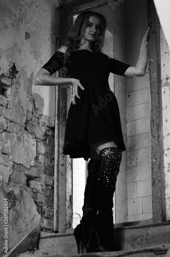 Young beautiful short hair blonde woman in black climbing the stairs, black and white photo. Side view of elegant romantic mysterious lady with movie star look in interior with bricks walls photo