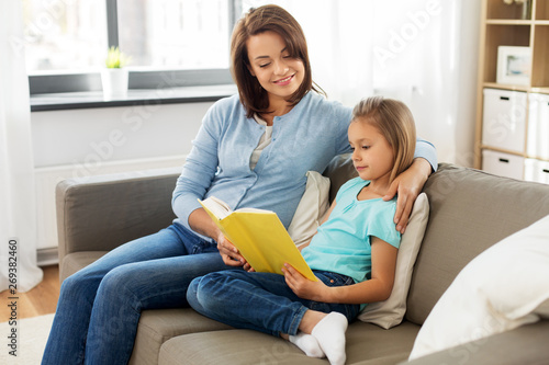 people, family and education concept - happy daughter with mother reading book at home