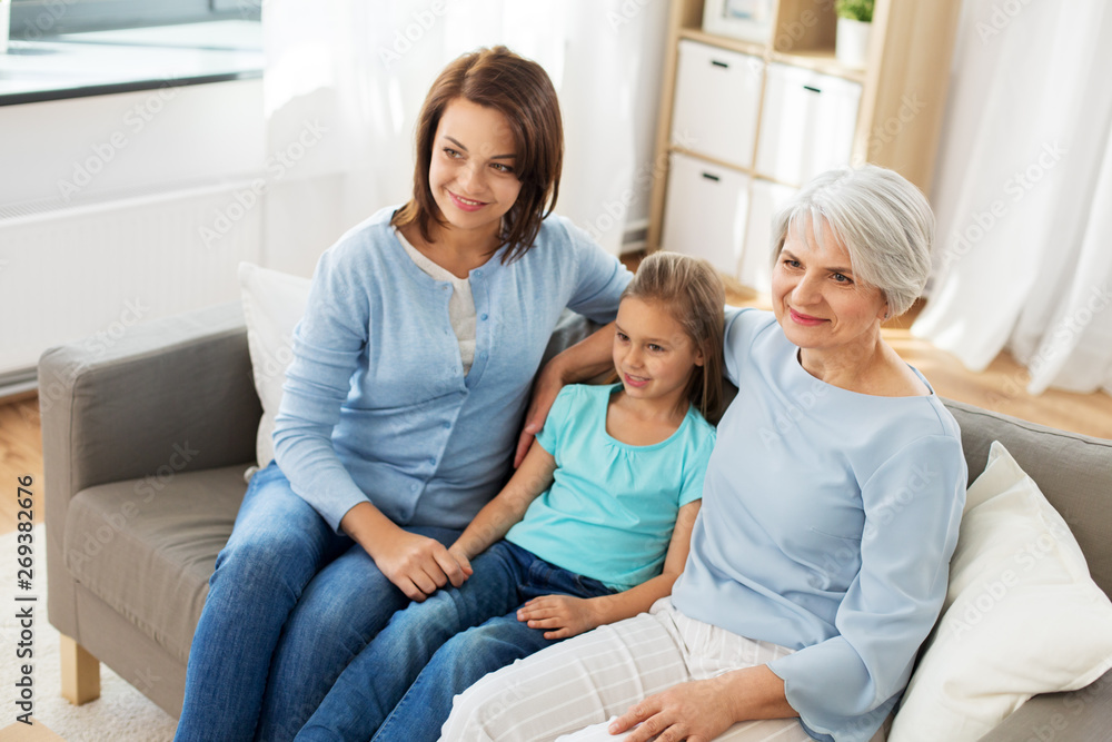 family, generation and female concept - portrait of smiling mother, daughter and grandmother sitting on sofa at home