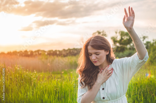 Fotografie Girl closed her eyes, praying in a field during beautiful sunset