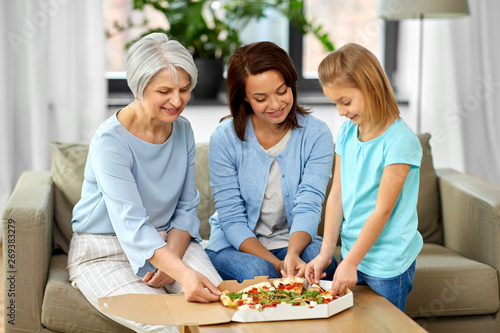 family  generation and female concept - smiling mother  daughter and grandmother sitting on sofa and eating takeaway pizza at home