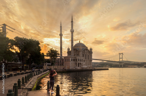 Ortakoy mosque on a beautiful summer day. Tourist girl is taking photos at sunrise.