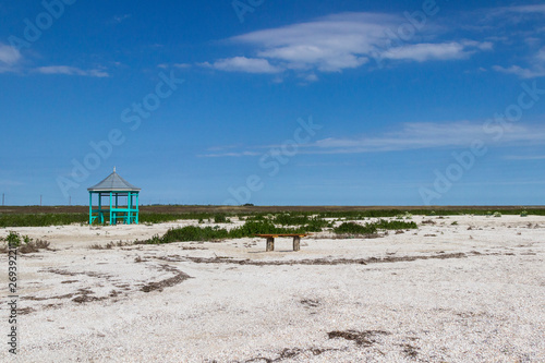 Wooden gazebo  and wooden bench in the steppe. Blue sky  land covered with small shells  steppe grass .