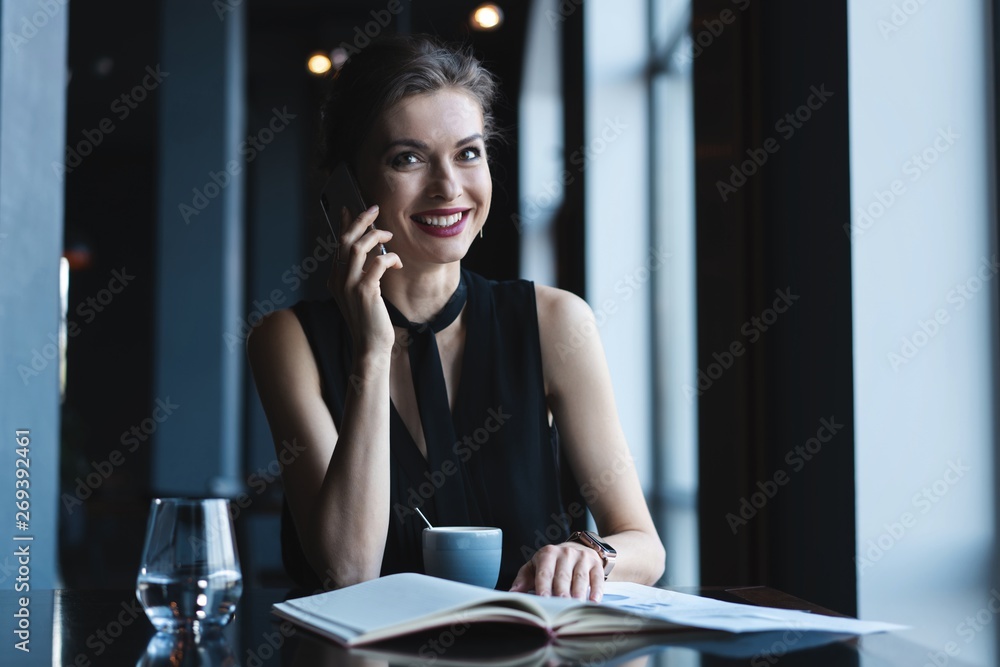 Young charming woman calling with cell telephone while sitting in coffee shop during free time, attractive female having talking conversation with mobile phone while rest in cafe. Young charming woman calling with cell telephone while sitting in coffee shop during free time, attractive female having talking conversation with mobile phone while rest in cafe.