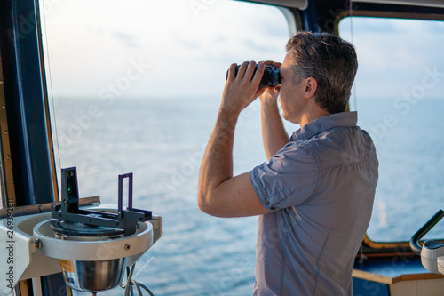 Navigational officer lookout on navigation watch looking through binoculars. Marine industry. COLREG collision regulations photo