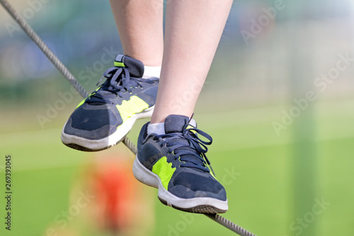 boy walking on tightrope closeup front view of kid feet in sneakers on steel rope against blurred background sport outdoor hiking activity authentic lifestyle concept natural color photo