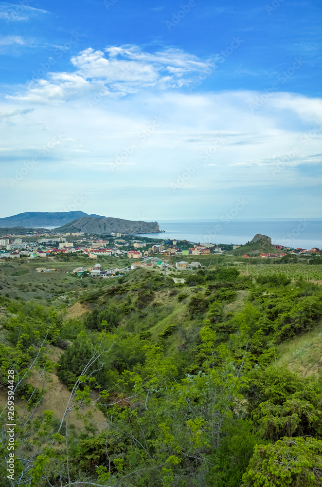 Sudak, Crimean Republic, Russia - May 30, 2017: View of the district of Sudak, residential buildings. Terrain in the mountains, vineyards, the sea on the horizon. View of Alchak mountain.