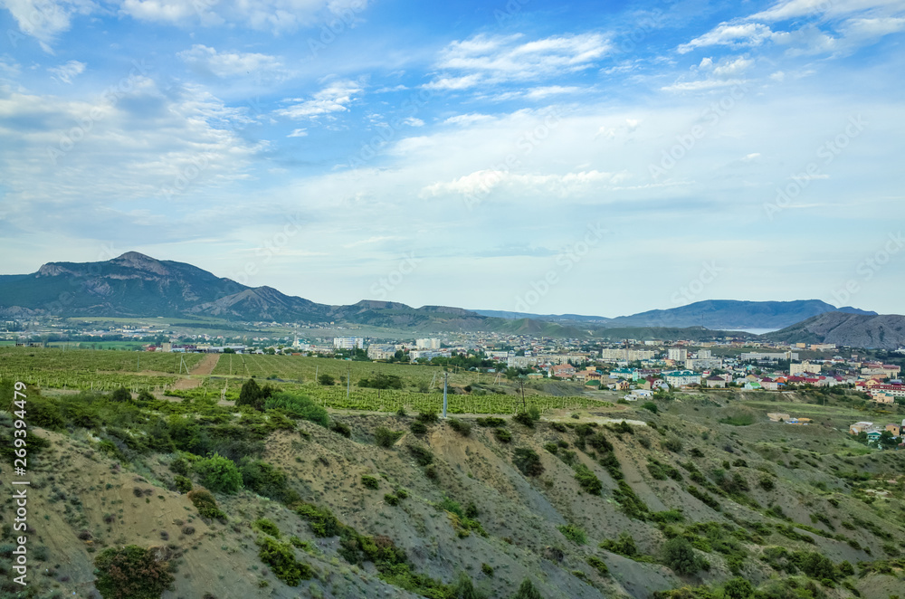 Sudak, Crimean Republic, Russia - May 30, 2017: View of the district of Sudak, residential buildings. Terrain in the mountains, vineyards, the sea on the horizon.