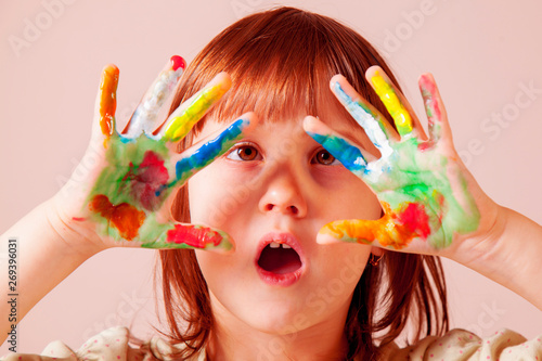 Funny portrait of cute little girl with painted in bright colors hands.