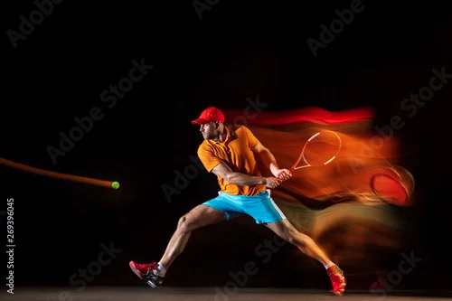 Obraz Jeden caucasian mężczyzna bawić się tenisa odizolowywającego na czarnym tle w mieszanym świetle. Studio strzał dysponowany młody męski gracz w ruchu lub akci podczas sporta gry. Pojęcie ruchu, sportu, zdrowego stylu życia.