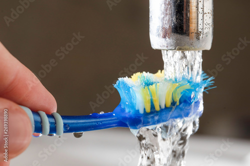 Tableau sur toile Washing a toothbrush in running tap water -  wastage of water.