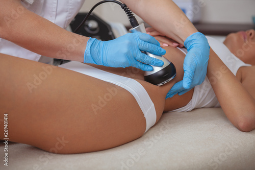 Cropped shot of a cosmetologist doing ultrasound cavitation procedure on the belly of a female client. Unrecognizable woman getting anti-fat treatment at beauty salon. Abdominal slimming concept photo